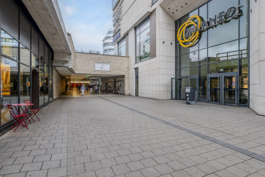 Eingang zum Milaneo Einkaufszentrum mit Glasfassade und gelbem Logo.