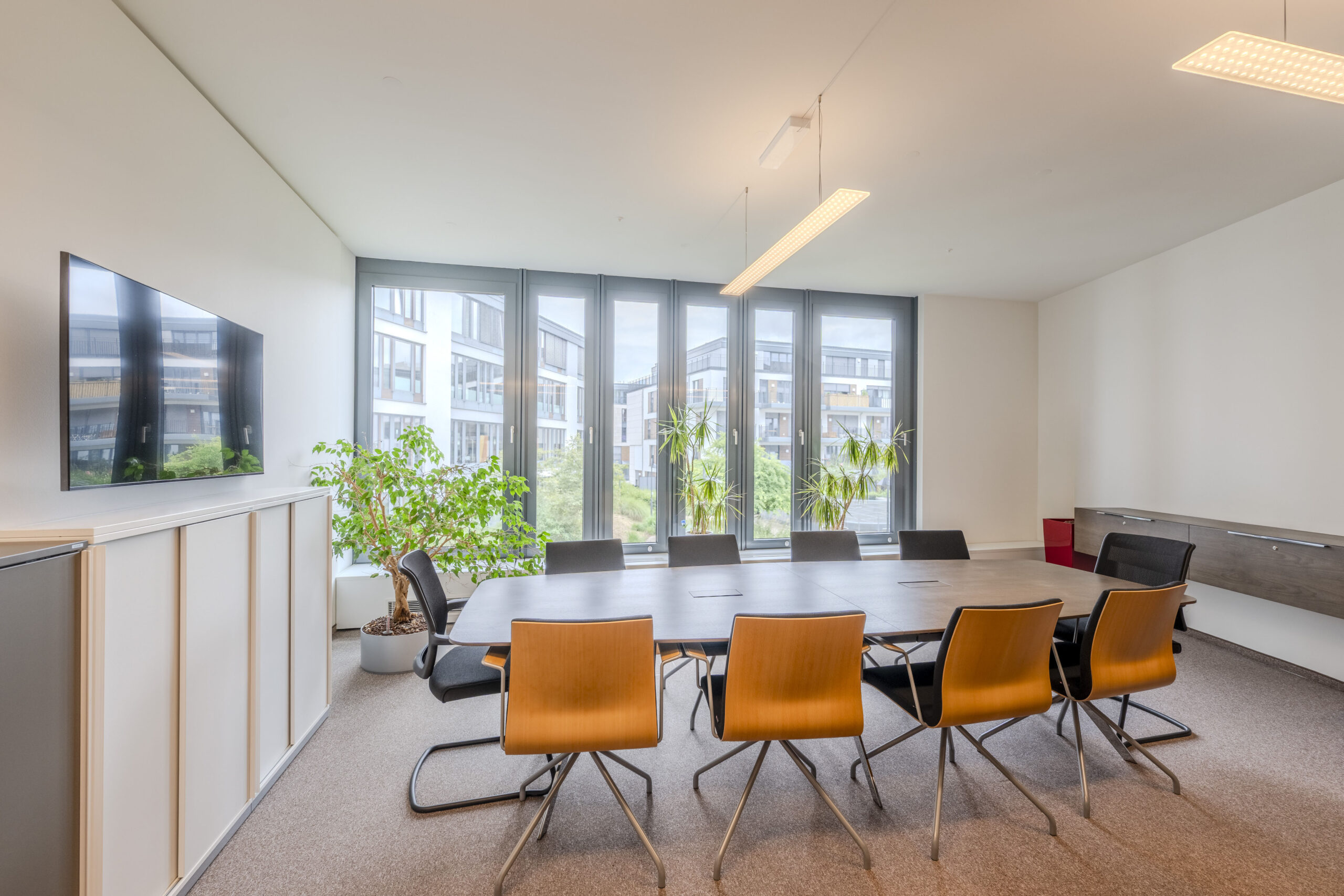 Konferenzraum mit Besprechungstisch, Stühlen und großem Bildschirm.