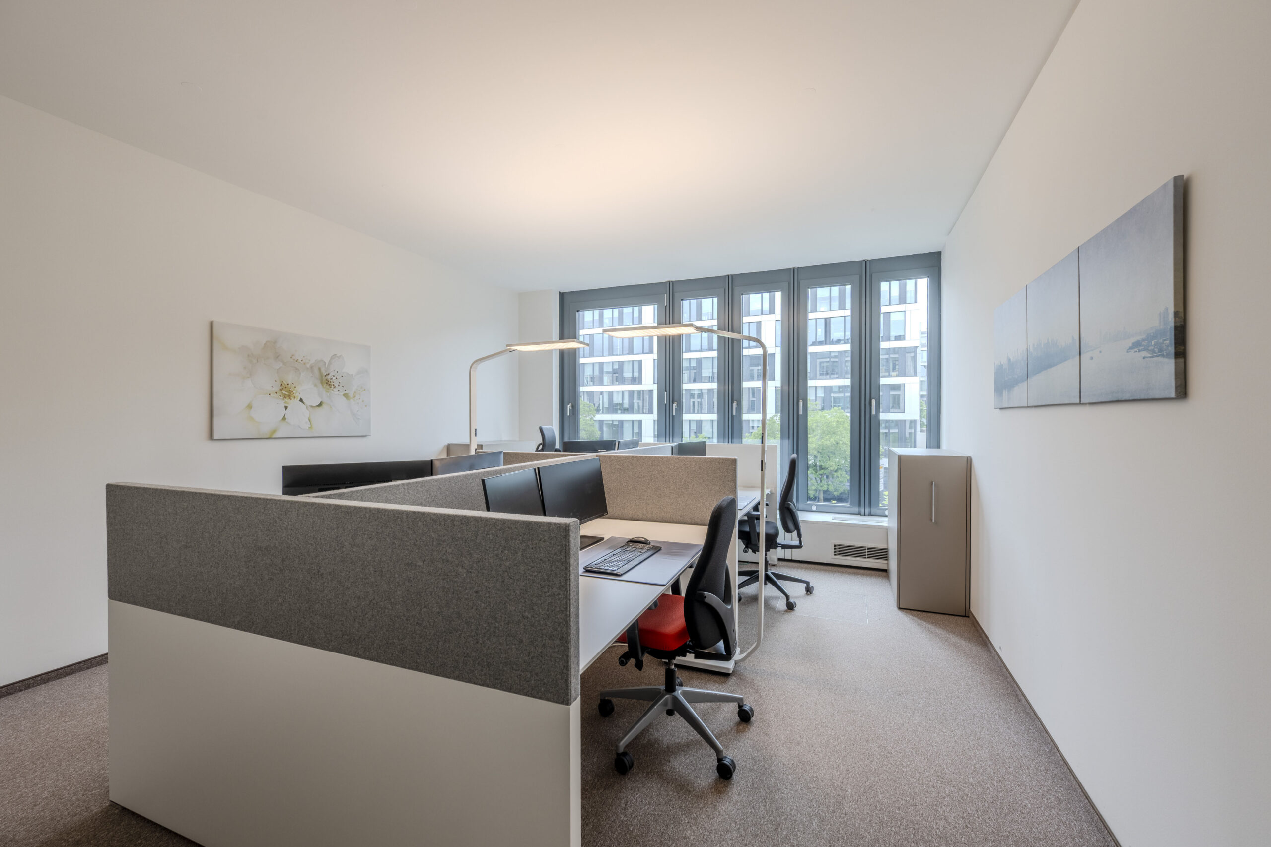 Arbeitsplatzbereich mit Schreibtischen, Monitoren und hohen Fenstern.