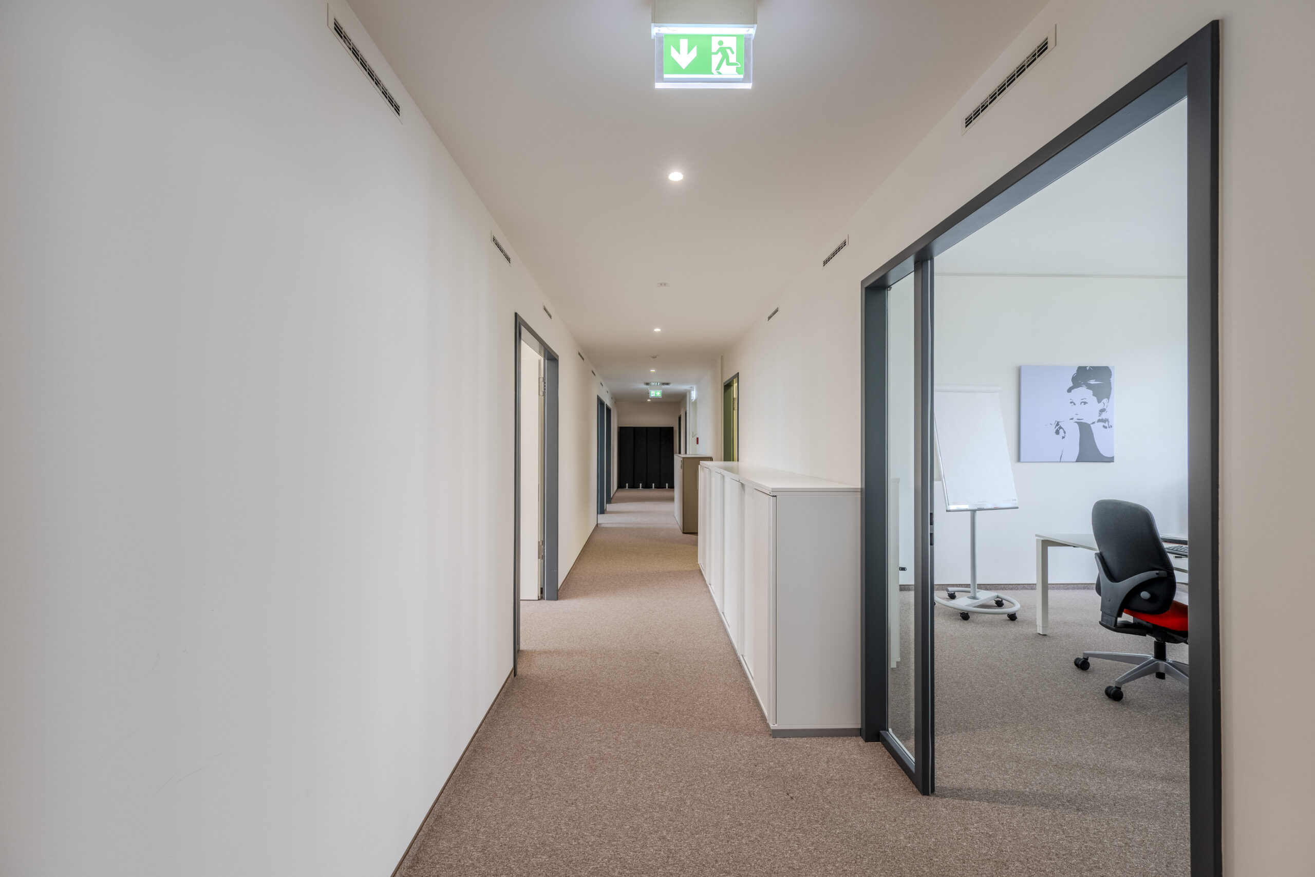 Langer Büroflur mit Glaswand zum Konferenzraum und seitlichen Bürotüren.