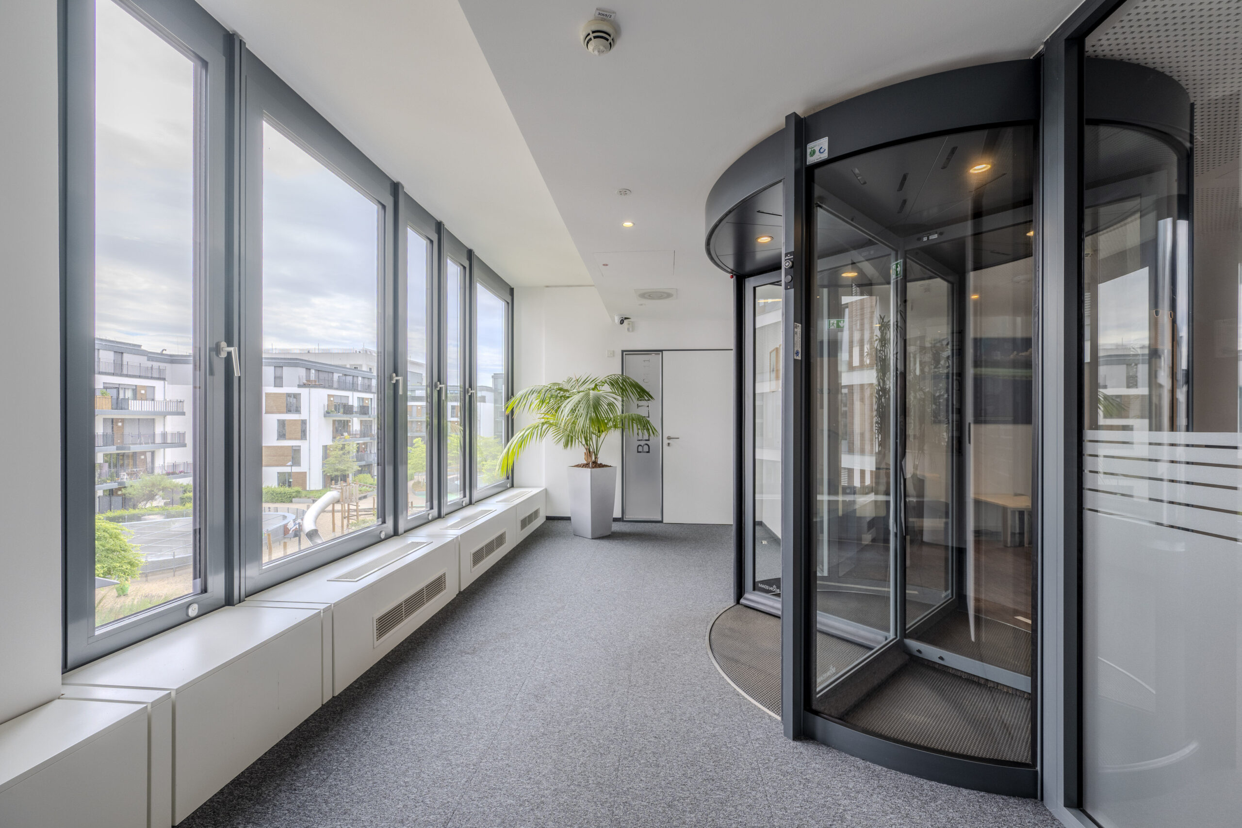 Eingangsbereich mit großen Glasfenstern und Drehtür.