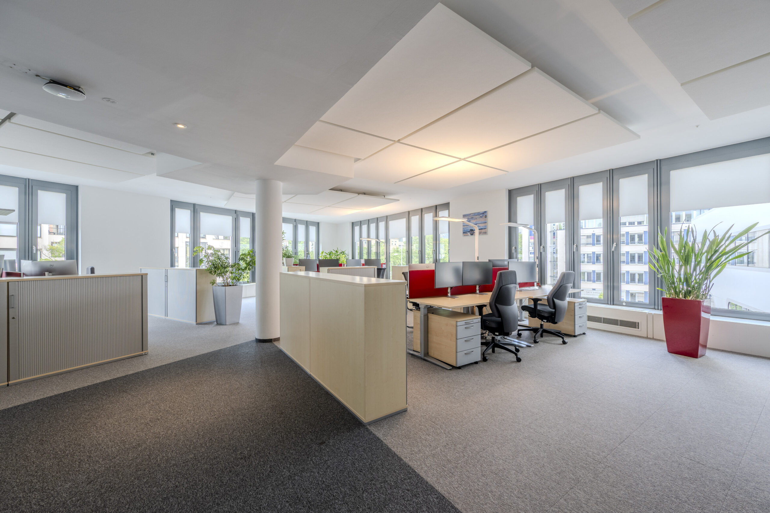 Helles Büro mit Arbeitsplätzen, Schreibtischen, Stühlen und großen Fenstern.